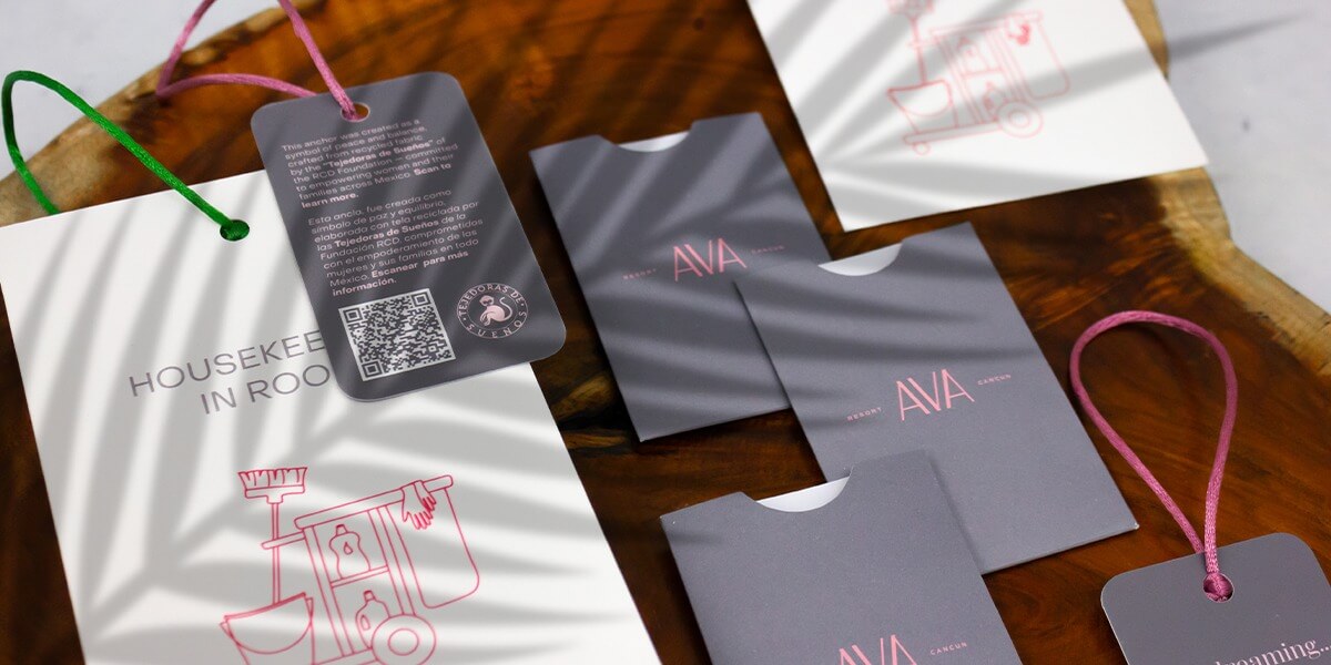 Papelería operativa diseñada y producida por Grupo Regio para AVA Resort Cancún, con llaveros y colgantes personalizados en tonos grises y rosas.