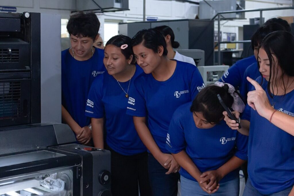 Grupo de jóvenes observa con interés una máquina de impresión en Grupo Regio, guiados por instructora.
