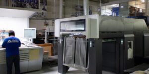 Operador de Grupo Regio revisando pruebas de color junto a máquina offset de alta tecnología en planta de impresión en Cancún.