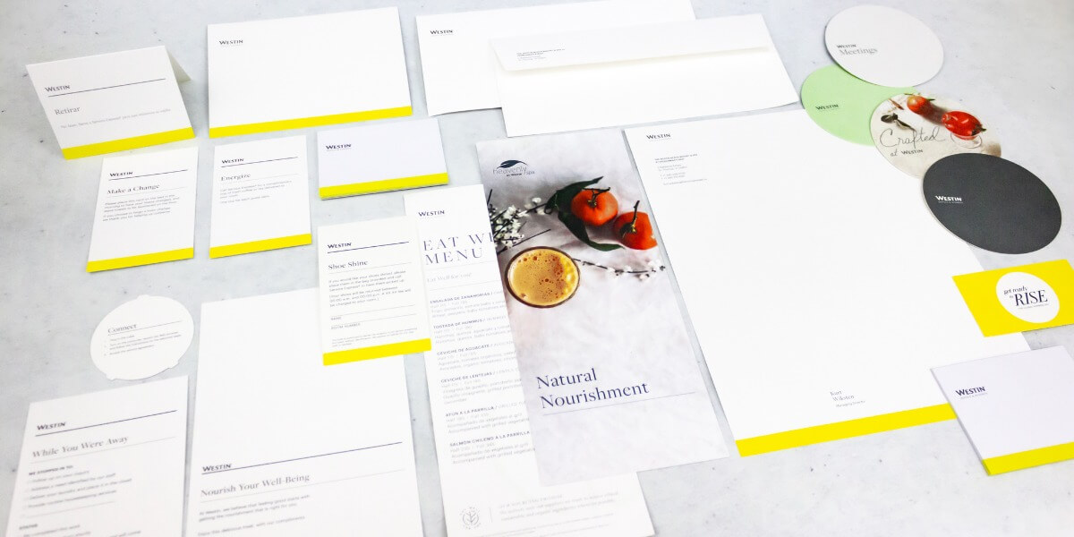 Imagen de papelería corporativa para Westin Hotels & Resorts, con sobres, cartas, menús y tarjetas impresas en diseño minimalista blanco con detalles en amarillo y gráficos gastronómicos, ejemplo de impresión hotelera de alta calidad en Cancún realizada por Grupo Regio.
