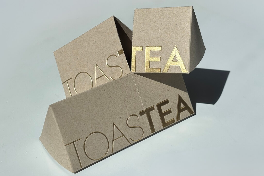 Empaque de cartón kraft para té con acabado de hot stamping dorado y diseño sustentable personalizado.