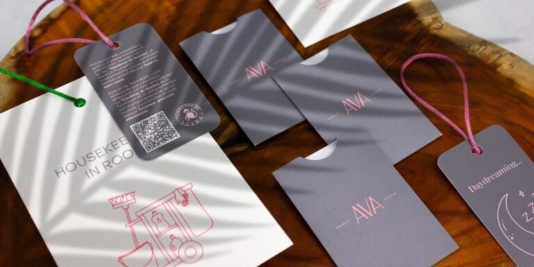 Imagen de papelería hotelera para AVA, con sobres para llaves en tono gris mate y colgantes de puerta con ilustraciones y textos en rosa, ejemplo de impresión personalizada y acabados de lujo elaborados por Grupo Regio en Cancún.
