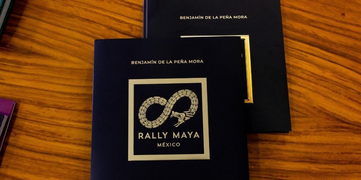 Imagen de libros con portada negra y estampado dorado del Rally Maya México, con tipografía elegante que incluye el nombre Benjamín de la Peña Mora, ejemplo de impresión editorial premium y acabados de lujo producidos en Cancún por Grupo Regio.