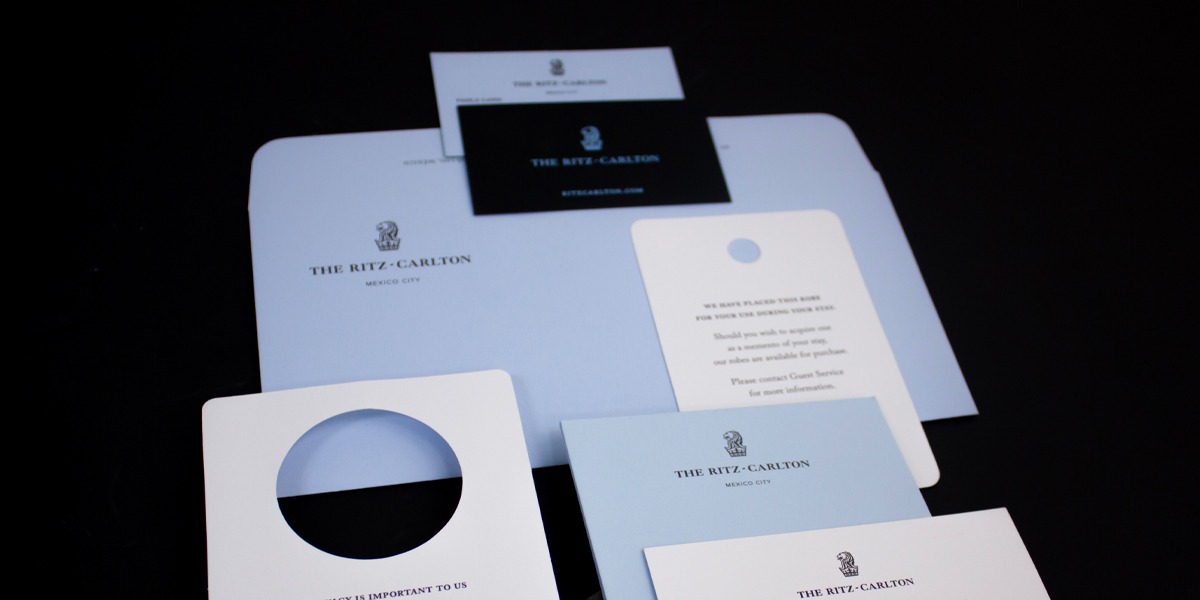 Papelería operativa impresa por Grupo Regio para The Ritz-Carlton Mexico City, con colgadores de puerta, carpetas y tarjetas en tonos blanco y azul, mostrando impresión premium para hotelería de alto nivel.