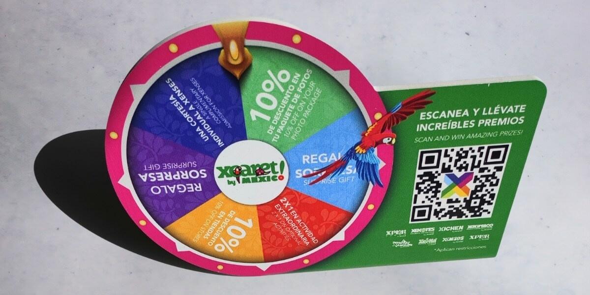 Display promocional impreso con ruleta de premios y código QR de Xcaret, diseño colorido para activación de marca.