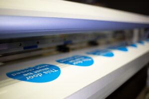 Máquina de Grupo Regio imprime etiquetas adhesivas azules con texto blanco para señalización corporativa.